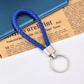 Portachiavi in pelle blu intrecciata con anello in metallo su sfondo di giornale - Blu scuro