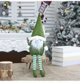Gnomo di Natale verde con gambe a strisce su uno sgabello di legno in un ambiente festivo - Verde
