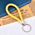 Bright yellow braided leather keychain with silver metal ring on vintage newspaper - Yellow