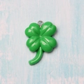 Green resin four-leaf clover charm with metal ring on light blue wood background - Clover with Screw Eye Pin