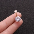 Close-up of a gold belly button ring with two clear round zircons held by fingers - Gold