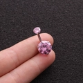 Pink round zircon belly button ring in silver stainless steel held between fingers - Pink