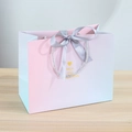 Détail d'un sac cadeau dégradé rose et bleu avec ruban et lettrage doré chic - Ruban Argent / Petit