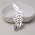 Matte silver feather brooch with dark grey pearl accent on a decorative dish - 0482-Silver Feather Pearl