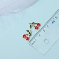 Macro shot showing exact size of 2.2cm red cherry charm with green leaves on scale - Cherry