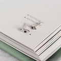 Detailed view of silver evil eye stud earrings with blue and white crystals on a book - Silver