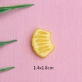 Makroaufnahme von 1,4x1,8cm gelbem muschelförmigem Harzanhänger auf rosa Hintergrund - Ananasfleisch