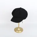 Detailed view of a classic black newsboy cap on a gold display stand with textured fabric - M (56-58cm) / Black