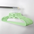 Detail of green plastic hangers with bow design and metal hooks on a laundry rod - Green Bow Shape