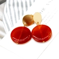 Detail view of red circular drop earrings with matte gold finish on textured background - Style 4 Ear Clip