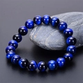 Close-up of natural blue tiger eye beads with cat-eye effect on a grey stone base - 10mm / Natural Blue Tiger Eye