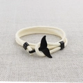 Detail of a beige woven bracelet featuring a black metal whale tail charm on fabric - Black Whale Tail Buckle / Off White