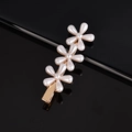 Close-up of three white pearl flowers on a gold metal hair clip over black reflective surface - Three Plum Blossoms