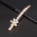 Macro shot of gold-plated hair clip featuring pearl flower design on a black reflective surface - Single Flower Curved Bobby Pin