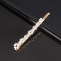 Close-up of golden pearl hair clip set on reflective black surface with clear texture - Twist Pearl Bobby Pin