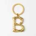 Detalle de un llavero de metal dorado con forma de letra B y textura de estilo bambú - Letra B