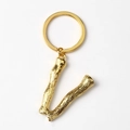 Detail of gold letter V keychain with realistic branch texture on a metal surface - Letter V