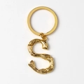 Macro detail of golden metal S-letter keychain with bamboo texture on white background - S