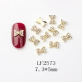 Vue macro de bijoux d'ongles nœuds dorés 7,3x5mm avec strass sur manucure rouge - Nœud en Alliage Doré Entièrement Strass (LF2573)