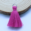 Deep pink cotton tassel with a silver metal ring accessory on a natural wood surface - Rose Red