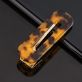 Macro shot of tortoiseshell acetate hair clip with gold metal base on black reflective surface - Acetate Amber Tortoise Square
