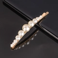 Detailed view of white pearls on a gold hair clip over a black reflective surface - Gradient Pearl Curved Bobby Pin