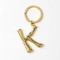 Detail of golden metal letter K keychain with unique branch texture on a white background - Letter K