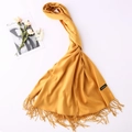 Detailed texture of yellow cashmere wool scarf with elegant tassels and brand label - Ginger Yellow