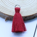 Red cotton tassel charm with silver metal ring on a textured wood background - Dark Red