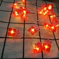 Detail view of red gift box LED string lights with warm yellow glow on checkered fabric - 1m 10-LED (2AA Battery Model) / Small Gift Box