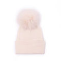 Detail of cream rib-knit baby hat with large faux fur pom-pom on white background - Beige