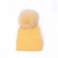 Close-up detail of a bright yellow knitted beanie featuring a large fluffy pom pom - Goose Yellow