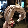 Detail of a champagne satin wide headband with a twisted knot design held by hand - Beige