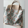 Stoff-Einkaufstasche mit Blumenmuster, Ledergriffen und Nieten auf modernem Stuhl - Blumendruck