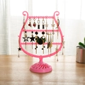 Pink harp-shaped jewelry organizer stand displaying diverse earrings on a wooden desk - Pink