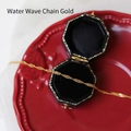 Macro detail of a golden water wave chain necklace draped over elegant gift packaging - Water Wave Chain / 45 cm / Gold