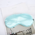 Light blue faux silk sleep mask with elastic strap placed on a lifestyle magazine - Lake Blue
