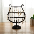 Harp-shaped black metal jewelry stand for earrings and necklaces on a wooden table - Black
