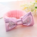 Detail of pink plush headband with large bow and embroidered Chic text on soft background - Pink
