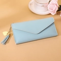 Detail of light blue envelope wallet with gold heart pendant and tassel on beige background - Long Style / Blue
