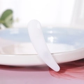 White plastic curved cosmetic spatula spoon for face cream on a luxury ceramic dish - White