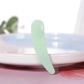 Single light green plastic crescent curved cosmetic spatula leaning on a ceramic plate - Dark Green