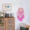Pink heart-shaped dreamcatcher with feathers and beads hanging in a cozy living room - Pink without Lights