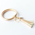 Detail of rose gold O-ring keychain with leather tassel and spring clip on white background - Champagne