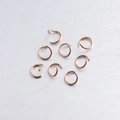 Detailed view of eight rose gold jump rings on a brushed grey metal surface for DIY jewelry - 1.2*10mm / Rose Gold