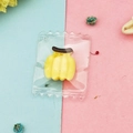 Nahaufnahme des Bananen-Harzanhängers in einer transparenten Miniatur-Verpackungstasche - Gelbe Banane