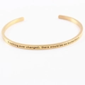 Detailed shot of golden stainless steel bracelet with engraved inspirational mantra text - if nothing ever changed, there would be no butterflies