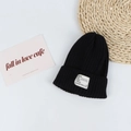 Close-up of black ribbed knit beanie with white textile patch and minimalist label detail - Head Circumference 50-58cm / Black
