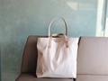 Close-up of white canvas tote bag with brown PU leather handles and metal rivet details - Cream