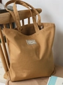 Detail einer braunen Canvas-Einkaufstasche mit weißem Webeetikett auf Holzstuhl - Camel